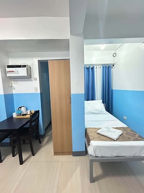 A hotel room with a bed, a desk, a chair, a wardrobe, and an air conditioning unit. - Metrohive Apartment 3B - Cozy Studio Near Airport & PITX (Pasay City)