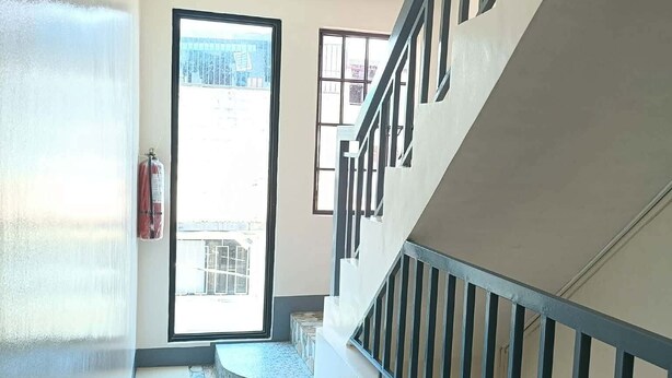Un corridoio con una scala, un estintore e una vista attraverso una porta.