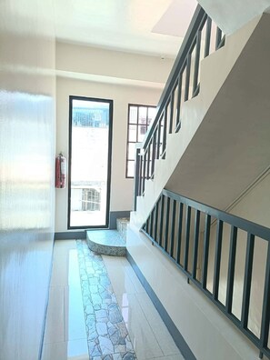 A hallway with a staircase, a fire extinguisher, and a view through a door. - Metrohive Apartment 3B - Cozy Studio Near Airport & PITX (Pasay City)