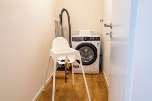 A compact laundry room with a washing machine, a drying machine, and a white chair. - Tide Resort 2nd Floor - Sauna. Balcony. Meernah. (Tossens)