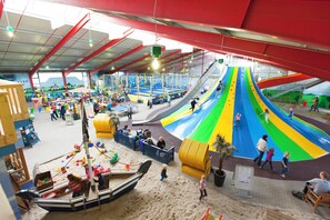 Ein Indoor-Spielbereich mit Rutschen, Sandkasten und verschiedenen Spielgeräten.
