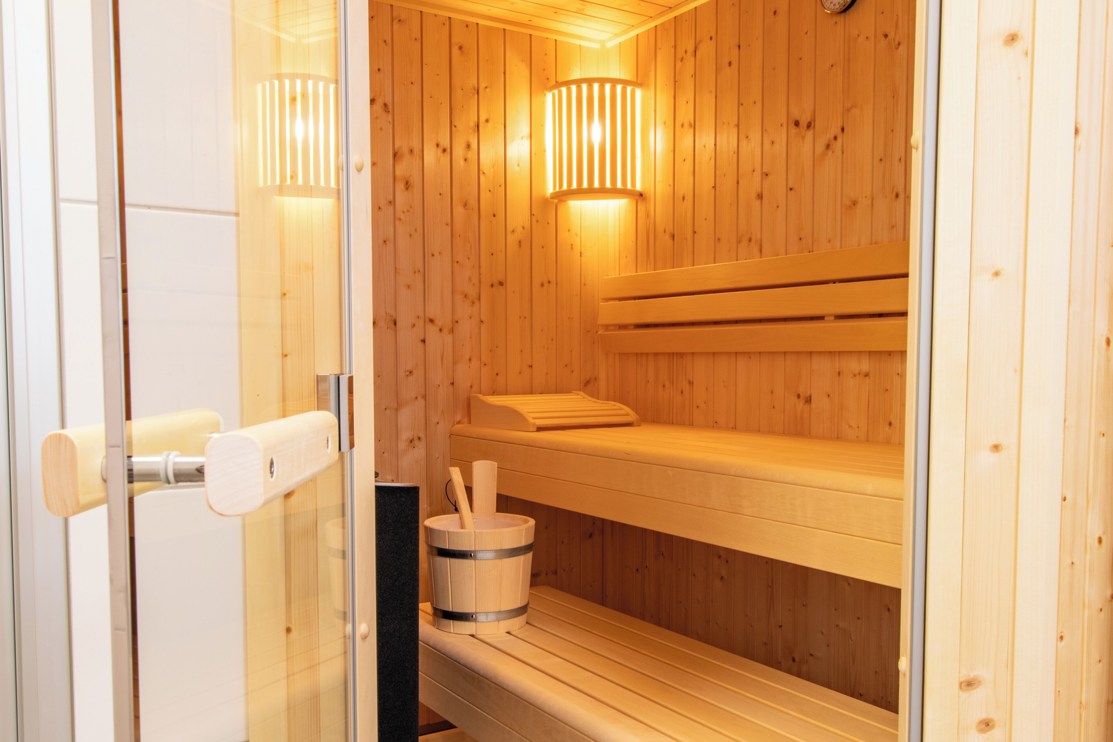 Una sauna con bancos de madera, un balde de madera y una puerta de cristal.