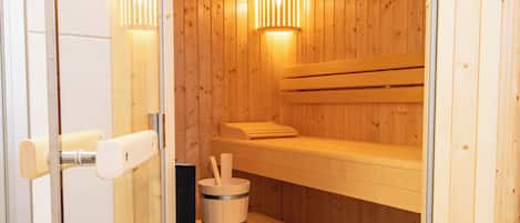 Una sauna con bancos de madera, un balde de madera y una puerta de cristal.