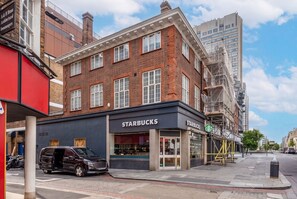 A Starbucks on a city street with a brick building facade, a parked car, and a clear sky. - Marble Arch's Gem - Large 2Bed 2Bath (London)