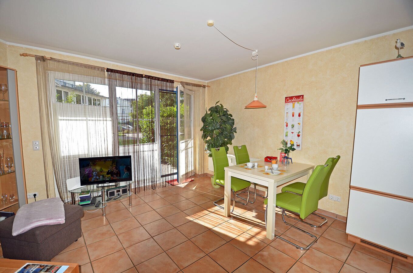 Un salon comprenant un téléviseur, une table à manger, des chaises, une plante et un réfrigérateur.