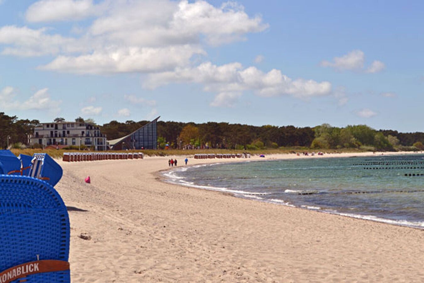 Ein Strand mit blauem Himmel, ein Gebäude mit geneigtem Dach und eine Reihe blauer Stühle.