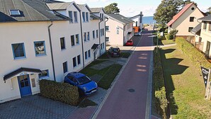 A residential street with houses, a blue car parked in front of one house, and a red car parked further down the street. - Just 50 meters from the sandy Baltic Sea beach, Wi-Fi, washing machine, accommodates up to 4 people, with a balcony (Glowe)