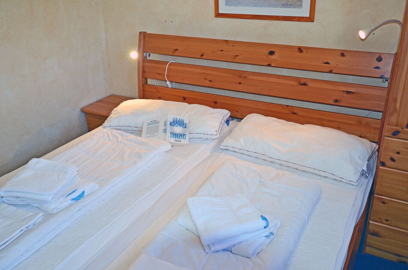 A double bed with white linens and pillows, a wooden headboard, and a bedside table with a lamp.