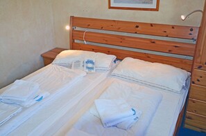 Een tweepersoonsbed met witte lakens en kussens, een houten hoofdbord, en een nachtkastje met een lamp.