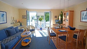 A living room with a sofa, dining table, chairs, and a view through a glass door to the outside. - Just 50 meters from the sandy Baltic Sea beach, Wi-Fi, washing machine, accommodates up to 4 people, with a balcony (Glowe)