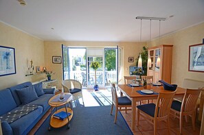 Ein Wohnzimmer mit einer Couch, einem Esstisch, Stühlen und Blick durch eine Glastür nach draußen.