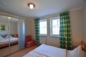 Ein Schlafzimmer mit einem Bett, einem roten Sessel, einem Spiegel und einem Fenster mit Vorhängen.