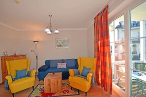 Un salon avec un canapé bleu, deux fauteuils jaunes, une table basse en bois et un lampadaire.