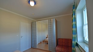 A bedroom with a bed, a wardrobe, a window with curtains, and a radiator. - Just 50 meters from the sandy Baltic Sea beach, Wi-Fi, washing machine, accommodates up to 4 people, with a balcony (Glowe)