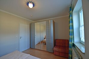Ein Schlafzimmer mit Bett, Kleiderschrank, Fenster mit Vorhängen und Heizkörper.