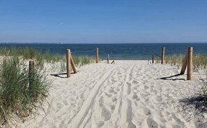 Ein sandiger Küstenweg führt zum Meer, gesäumt von Holzbefestigungen und Gras.