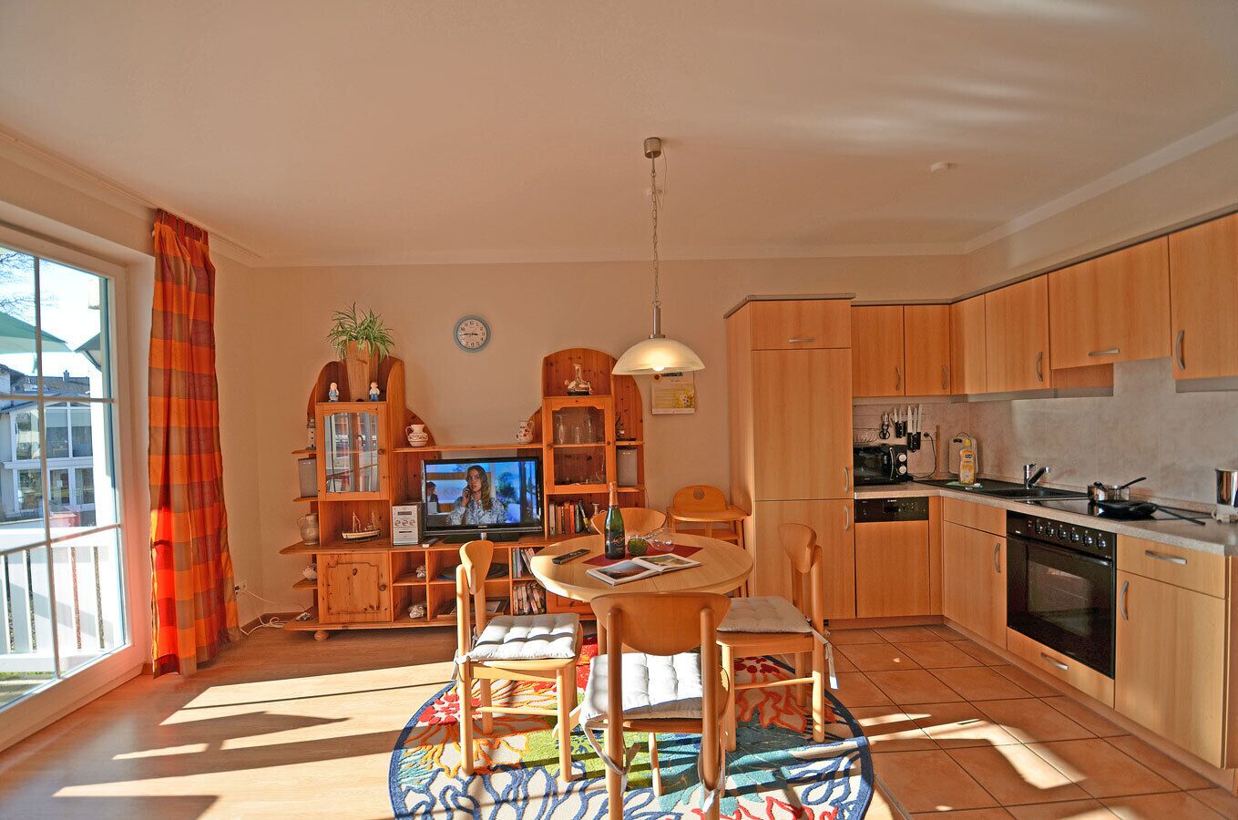 A well-lit, open-plan living and dining area with a kitchen, a television, and a dining table with chairs.