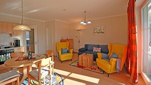 A living room with a sofa, chairs, a dining table, and a kitchen in the background. - Just 50 meters from the sandy Baltic Sea beach, Wi-Fi, washing machine, accommodates up to 4 people, with a balcony (Glowe)
