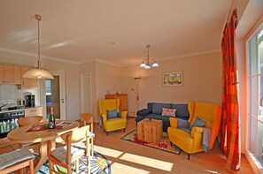 Ein Wohnzimmer mit Sofa, Sesseln, einem Esstisch und einer Küche im Hintergrund.