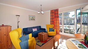 A living room with a sofa, two armchairs, a coffee table, and a dining table with chairs. There is a window with a view of buildings outside. - Just 50 meters from the sandy Baltic Sea beach, Wi-Fi, washing machine, accommodates up to 4 people, with a balcony (Glowe)