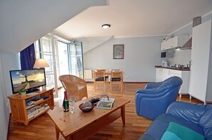 Ein Wohnzimmer mit Fernseher, einem Holztisch, einem blauen Sofa und einem Essbereich mit Tisch und Stühlen.