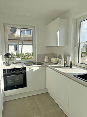 A modern kitchen with white cabinets, a built-in oven, a coffee maker, and a window providing natural light. - Fully fenced, located between the Bodden and a natural beach, with a sauna and internet access (Dranske)