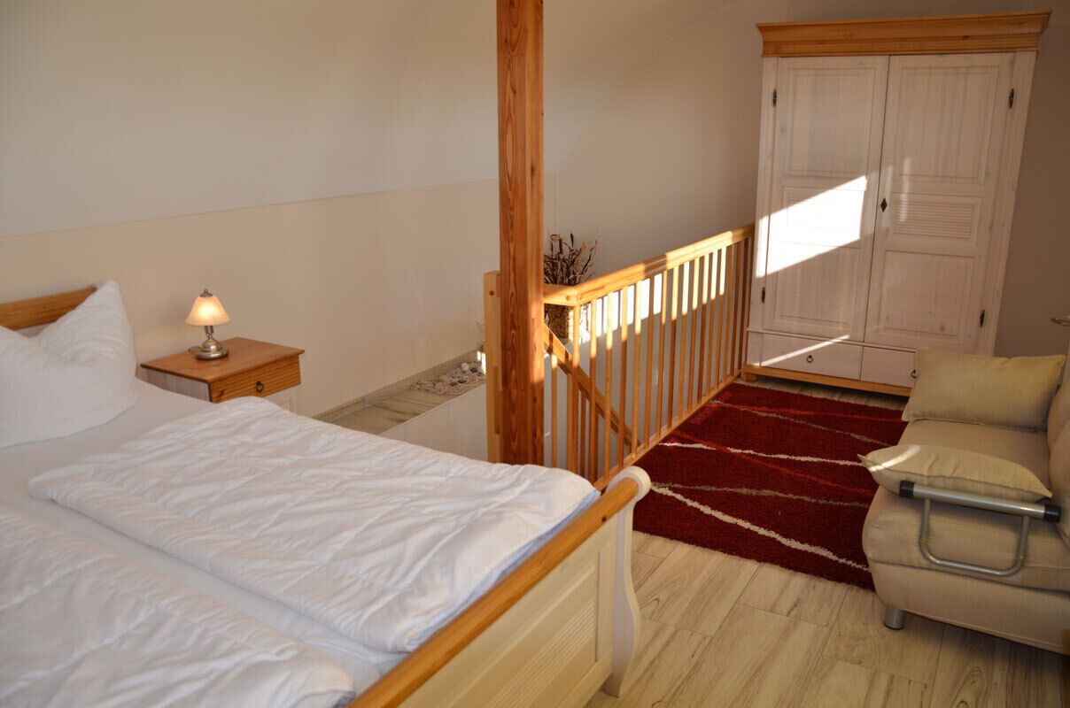A bedroom with a bed, nightstand, lamp, wooden staircase, and a wardrobe.
