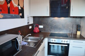 A modern kitchen with a built-in oven, a stainless steel sink, and a red kettle on the countertop. - Cozy furnishings, close to the beach, just 100 m from the sandy beach, balcony, pets allowed (Juliusruh)