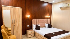 A bedroom with a wooden wardrobe, a bed with white bedding and brown pillows, a bedside table, and a nightstand. - The Shree Heritage And Rooftop (Bara Banki)