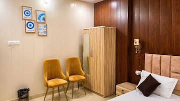 A hotel room with a bed, two chairs, a wardrobe, and wall art.