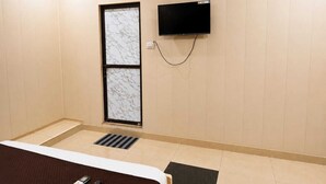 A hotel room with a bed, a television mounted on the wall, and a window with a marble-like pattern. - The Shree Heritage And Rooftop (Bara Banki)