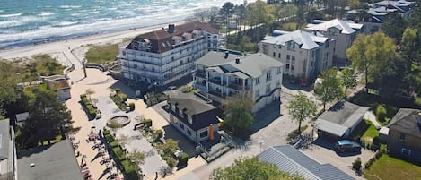 Eine Vogelperspektive auf ein Küstenwohngebiet mit mehreren Gebäuden, einem Strand und einem Parkplatz.