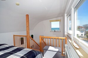 A bedroom with a bed, a window with a view of the sea, a small window, and a wooden staircase. - Cozy and comfortable, just 100 meters from the sandy beach, ocean view, balcony, pets allowed (Juliusruh)