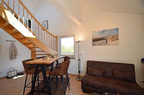 A room with a wooden staircase, a dining table with chairs, a sofa, and a painting on the wall. - Cozy and comfortable, just 100 meters from the sandy beach, ocean view, balcony, pets allowed (Juliusruh)