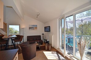 A modern living room with a sofa, a coffee table, and a TV mounted on the wall. - Cozy and comfortable, just 100 meters from the sandy beach, ocean view, balcony, pets allowed (Juliusruh)