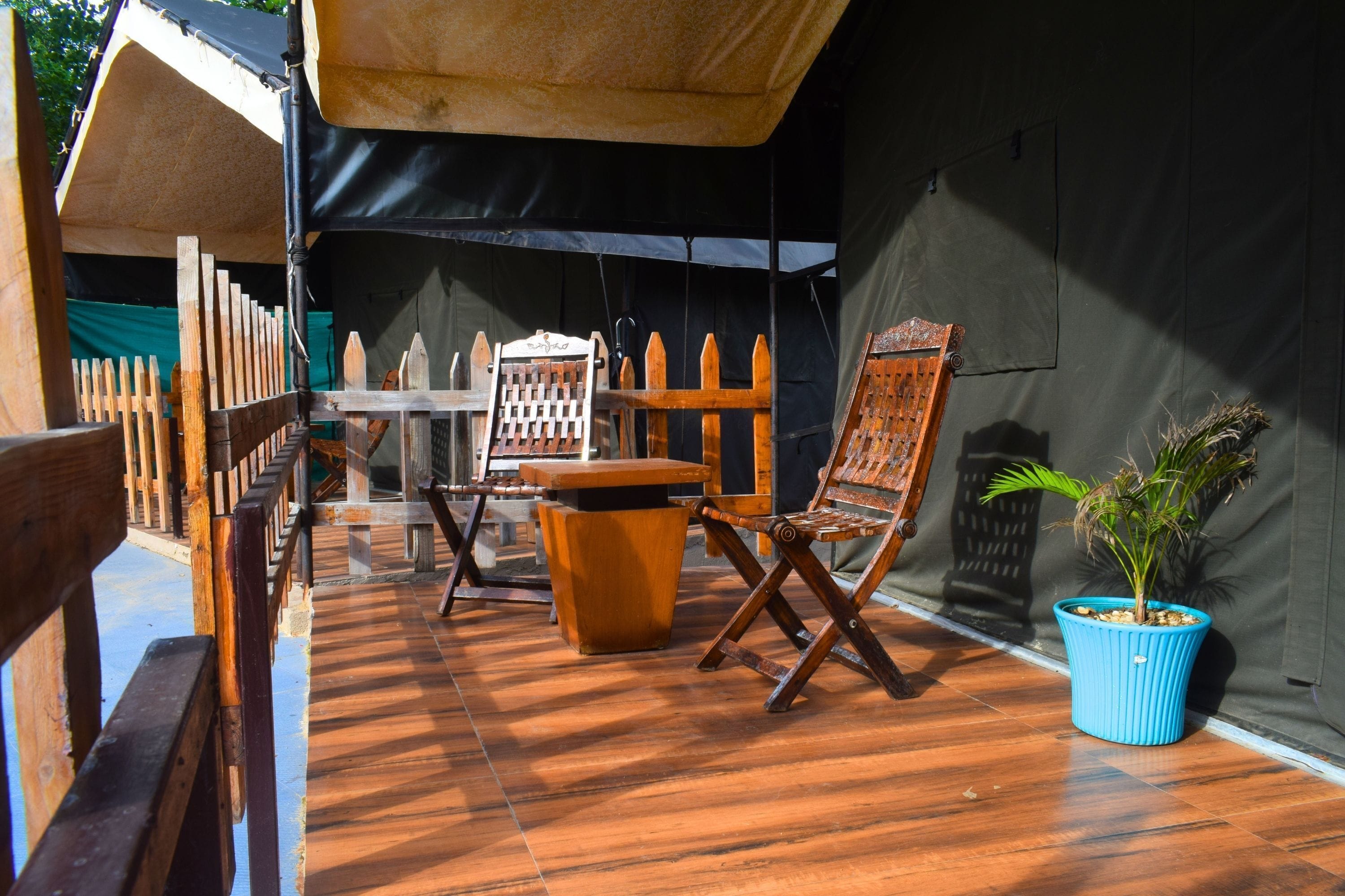 Un espacio de estar al aire libre cubierto, con mobiliario de madera y una planta en maceta.
