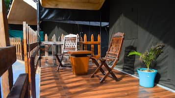 Un espacio de estar al aire libre cubierto, con mobiliario de madera y una planta en maceta.