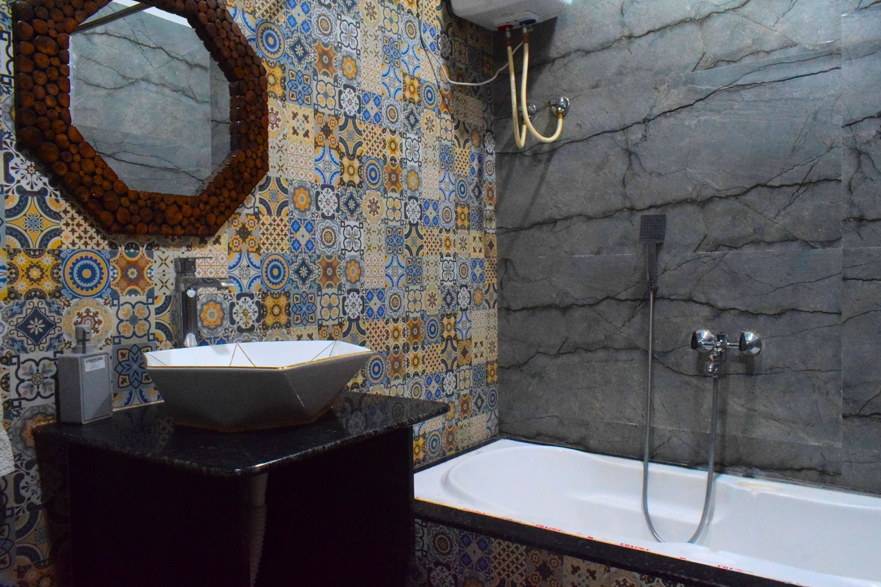 Un baño con pared de azulejos, un lavamanos, un espejo y una bañera.