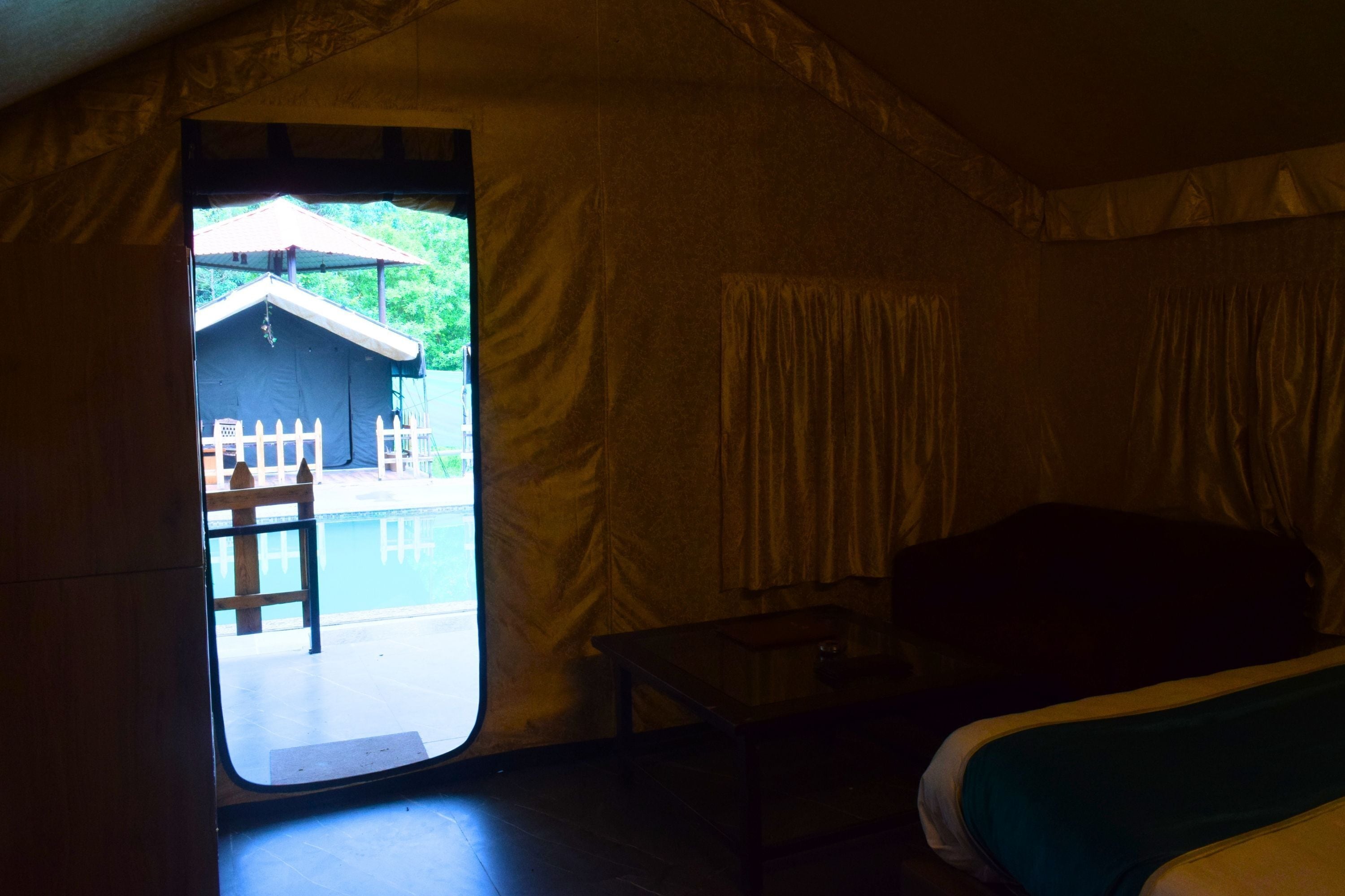 Un alojamiento en tienda de campaña con cama, una mesita y vistas a una piscina y un edificio.