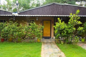 A building with a checkered pathway leading to a wooden door, surrounded by lush greenery and potted plants.