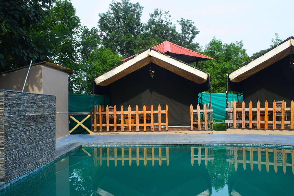 A swimming pool with two wooden cabins, a stone wall, and a wooden fence.