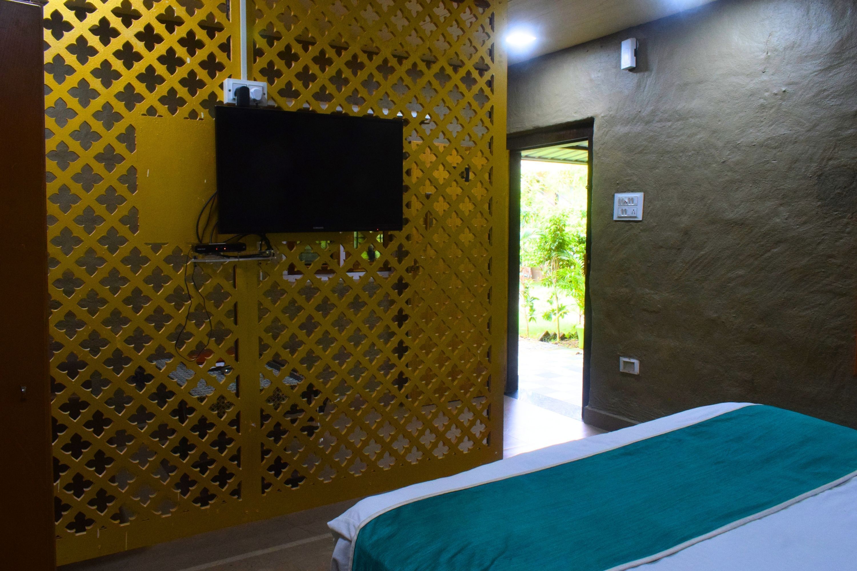 Una habitación con una cama, un televisor montado en un panel amarillo con motivos y una puerta que da al exterior.
