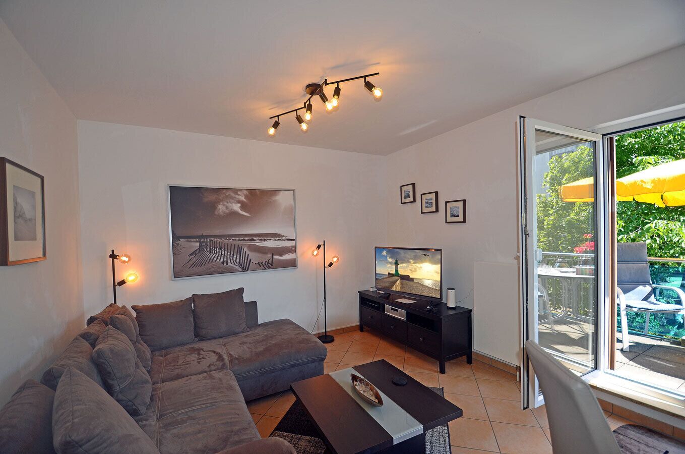 Ein modernes Wohnzimmer mit einer Couch, einem Flachbildfernseher, einem Couchtisch und einer Deckenleuchte.