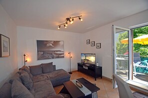 Un salon moderne comprenant un canapé, un téléviseur à écran plat, une table basse et un luminaire suspendu au plafond.