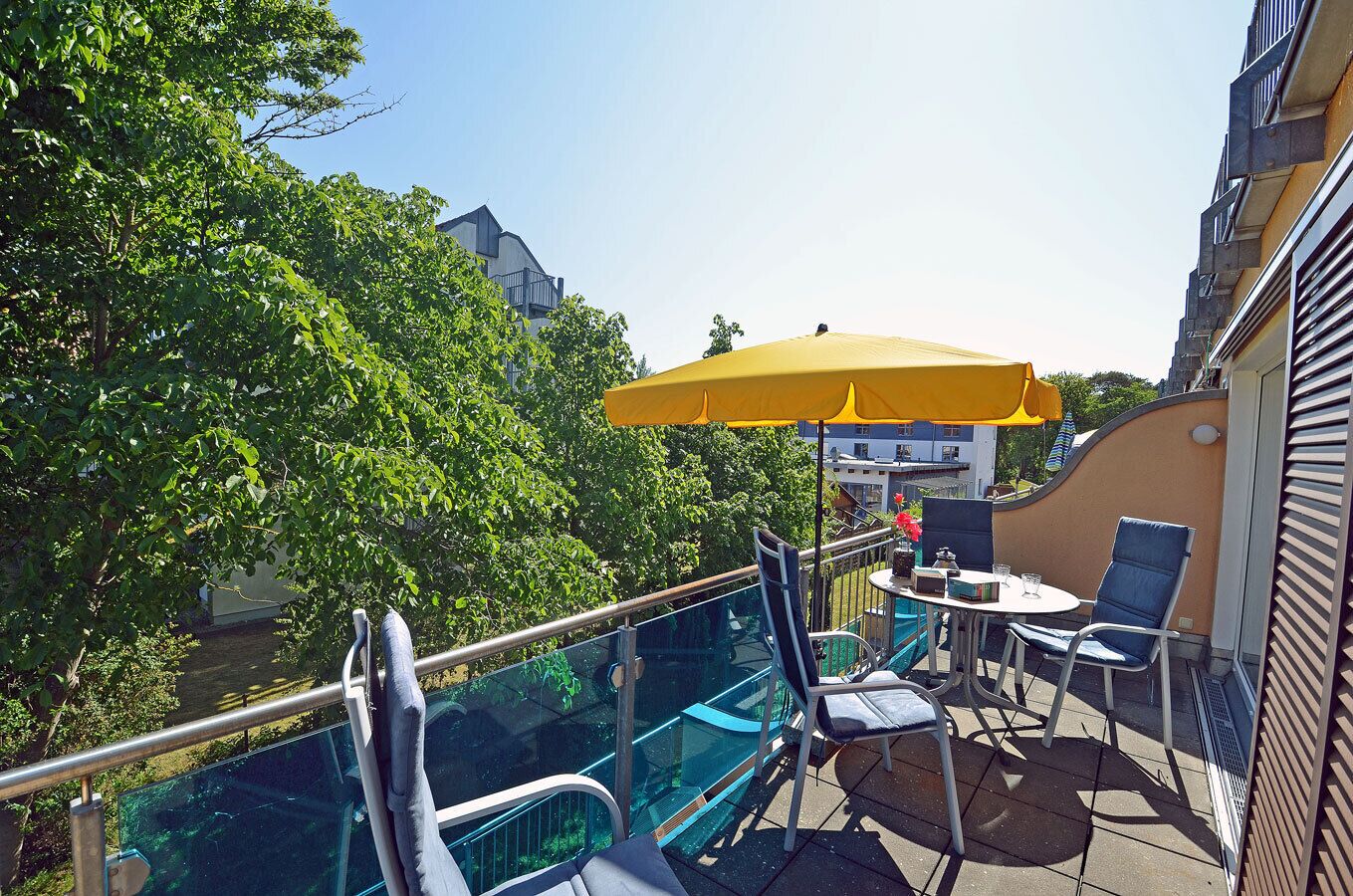 Ein Balkon mit Glasgeländer, Sitzgelegenheit im Freien und einem gelben Sonnenschirm.