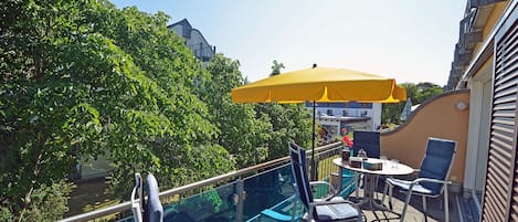 Un balcon doté d’une barrière en verre, d’un espace salon extérieur et d’un parasol jaune.