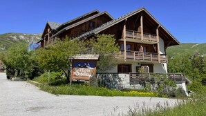 A wooden chalet with a balcony, surrounded by greenery and a clear sky. - Cozy apartment with balcony - 4 guests (La Toussuire)