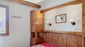 A wooden-paneled room with a bed, a wall-mounted light fixture, and a framed picture. - Cozy apartment with balcony - 4 guests (La Toussuire)