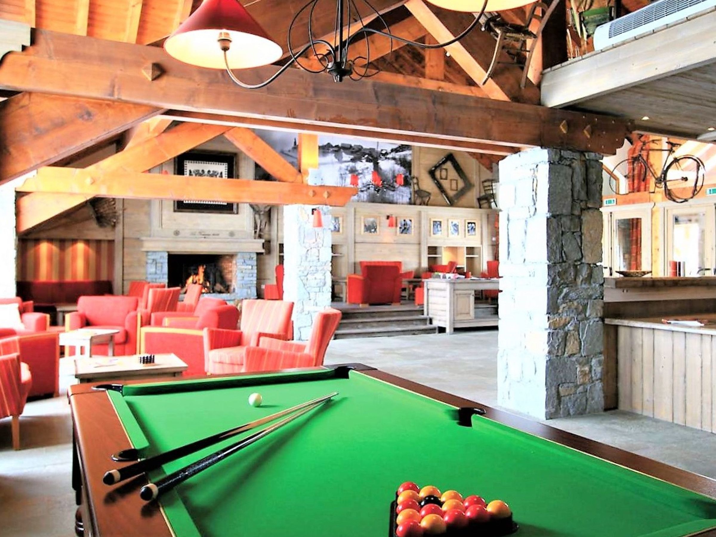 A pool table in a room with red chairs and a fireplace.