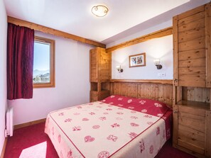 Habitación con cama, cabecera de madera, ventana con vistas y una lámpara fijada a la pared.